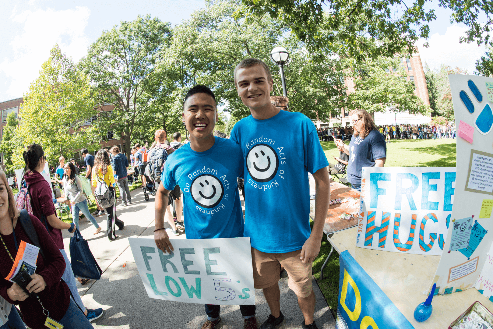Smiling students on the Diag holding a "free hugs" sign.